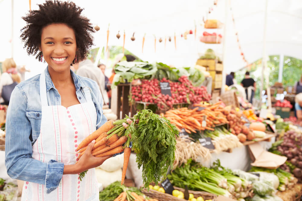 woman holding carrots with a produce stand behind her